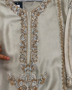 Close-up of a beige or champagne-colored embroidered garment, likely a kurta or tunic, featuring ornate metallic silver and gold floral embroidery around the neckline and lower front panel.