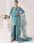 A woman models a teal blue three-piece salwar kameez suit with matching dupatta. The kurta and wide-leg trousers feature gold and silver embroidery, and the sheer dupatta has matching floral patterns.