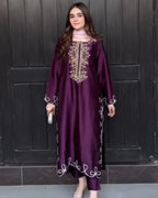 A woman wearing a long-sleeved deep purple kaftan dress with gold and white embroidery, standing in front of a dark paneled door.