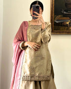 A woman takes a mirror selfie wearing a beige embroidered traditional outfit with a dusty pink dupatta draped over her shoulder. The outfit features a beige kurta with silver and gold embroidery, and the pink dupatta has subtle gold accents.