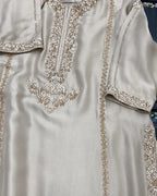 A close-up of a light beige or champagne-colored satin kurta featuring intricate silver and gold embroidery around the neckline, sleeve cuffs, and front panel.
