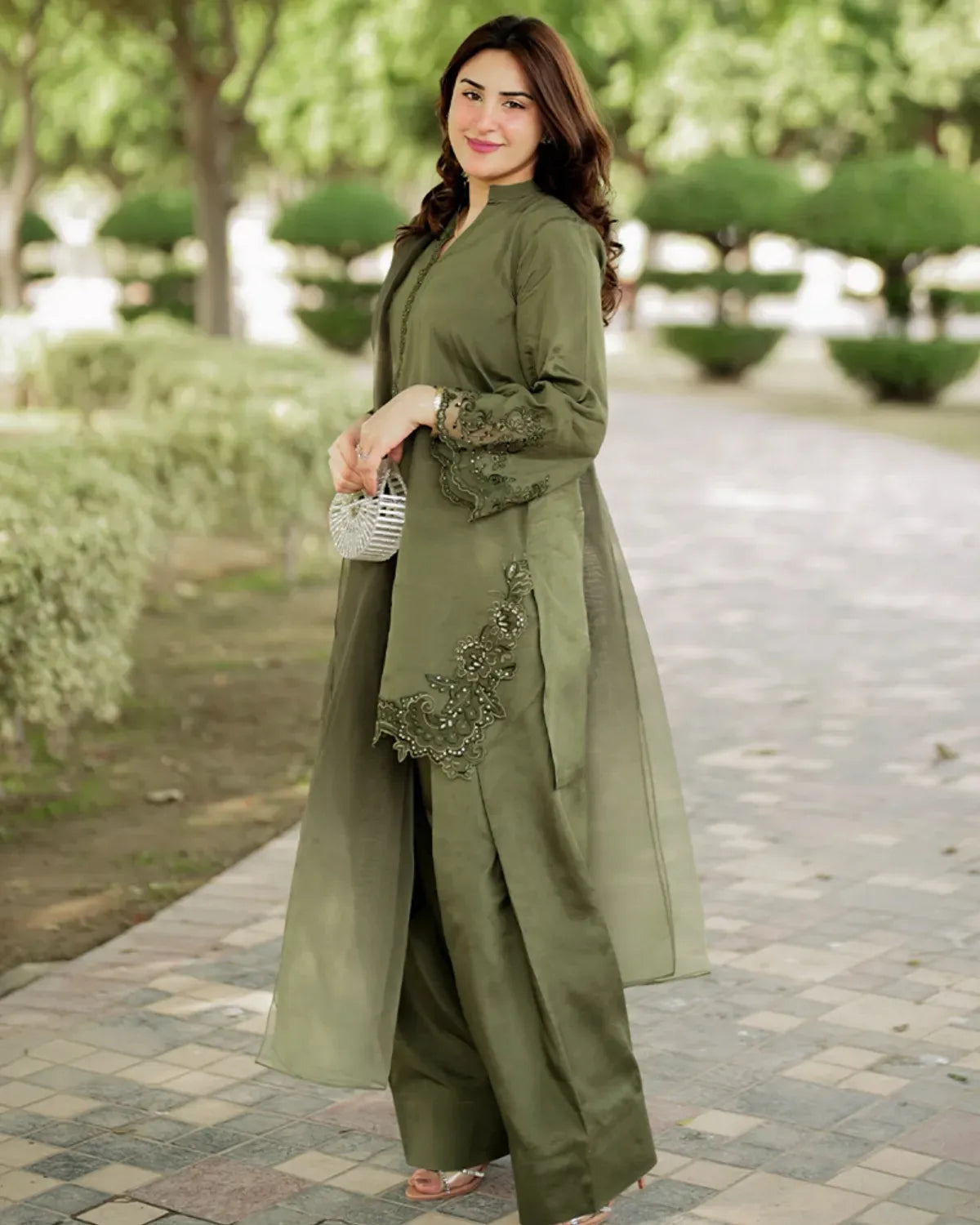 Woman in a green outfit with floral embroidery standing in a park.