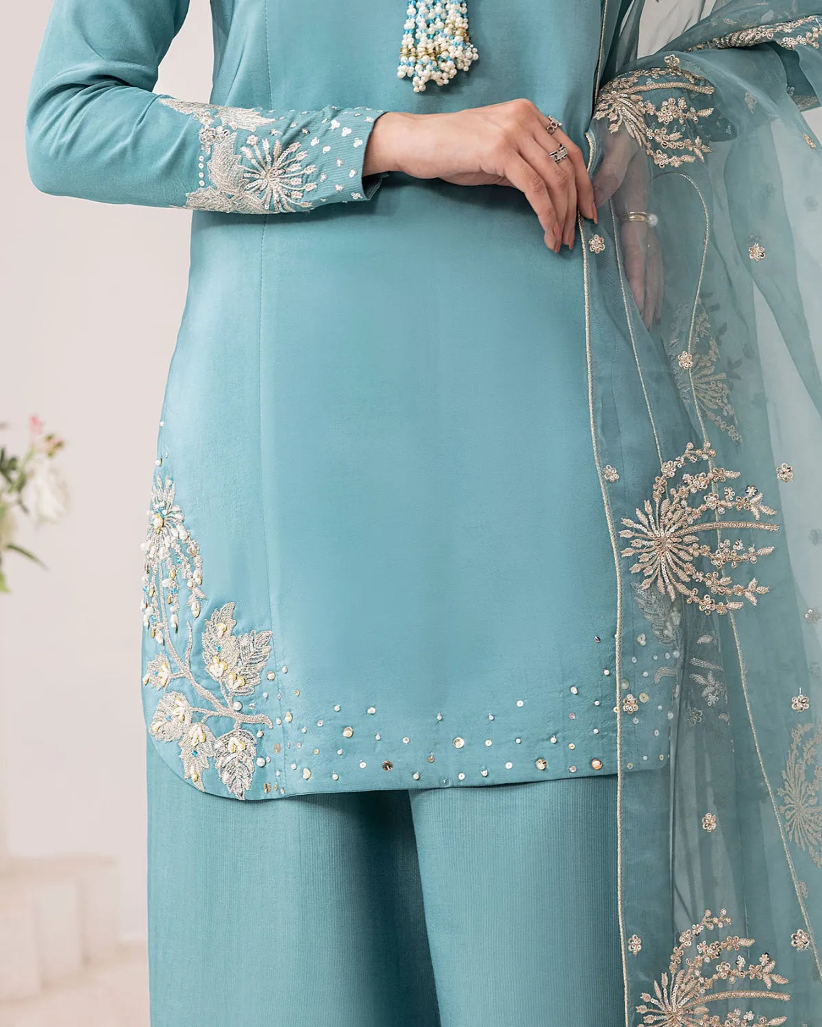 A close-up of a person wearing a light blue traditional outfit with embroidered details on the kurta and matching pants, along with a sheer dupatta draped over one shoulder.
