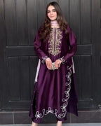 A woman wearing a long, deep purple embroidered dress with white and gold detailing, standing in front of a dark paneled door.