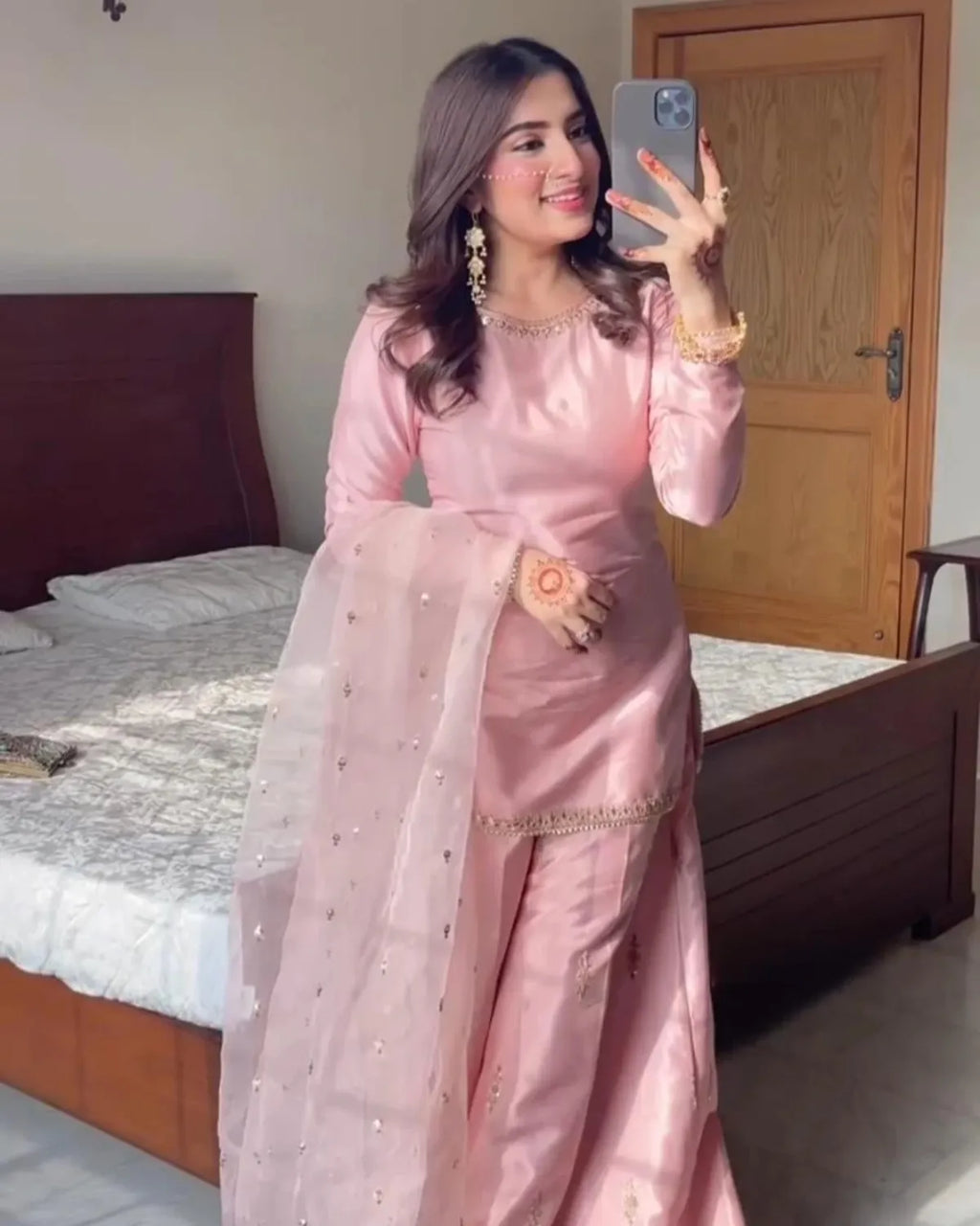 Woman in a pink traditional outfit taking a mirror selfie in a bedroom.
