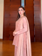 A woman modeling a dusty pink traditional outfit with a matching long draped scarf, standing in front of a wooden door and wooden floor.